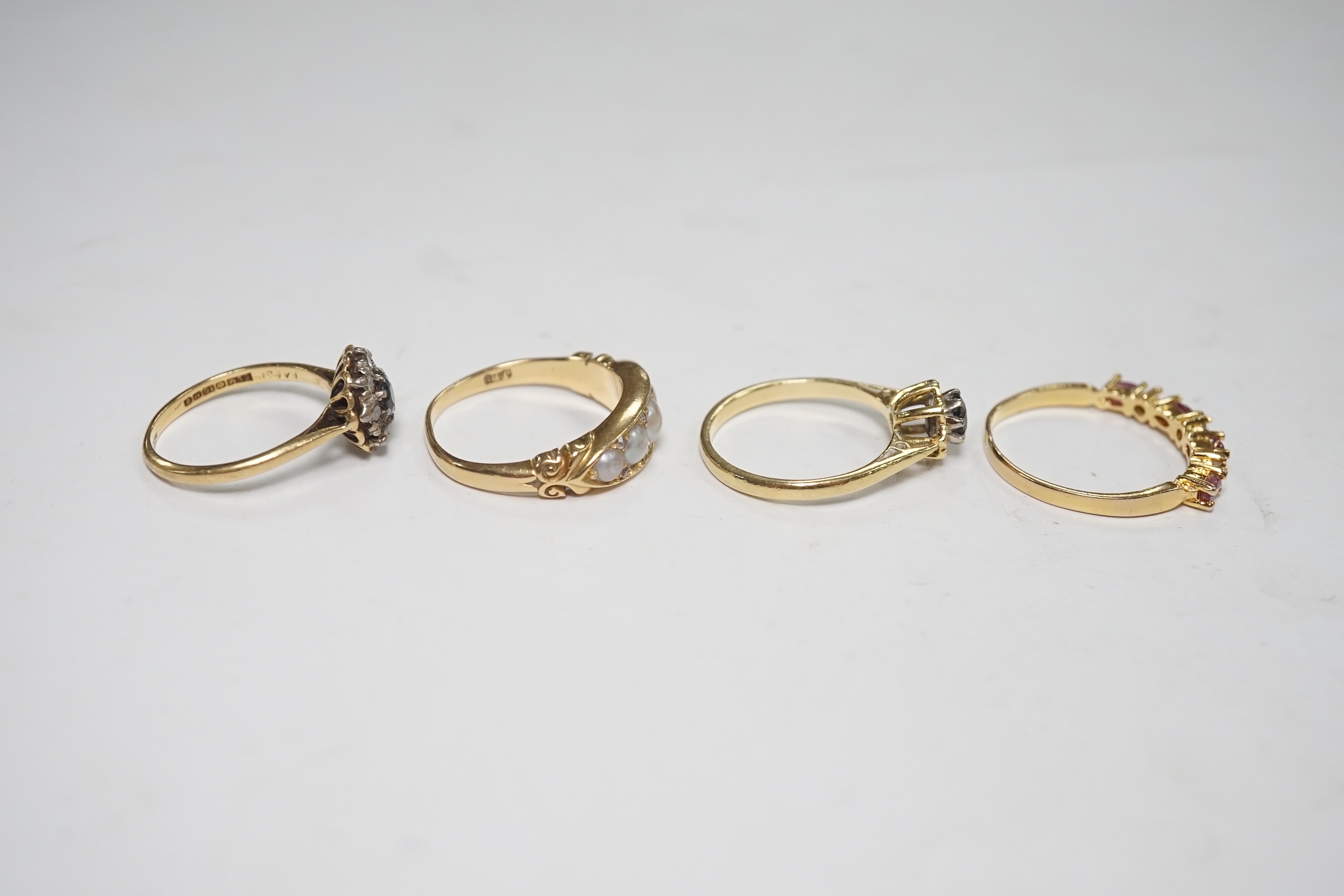 A late Victorian yellow metal and five stone split pearl set half hoop ring, with diamond chip spacers, size N/O, two modern 18ct gold and gem set rings and one other ring. Condition - fair to good